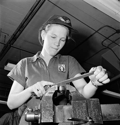 Woman factory worker files a machine part while piped music plays on loudspeakers.  / Une ouvrière d’usine lime une pièce de machine pendant que des hauts-parleurs diffusent de la musique